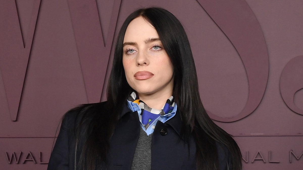 Billie Eilish standing in front of a maroon background at an awards event