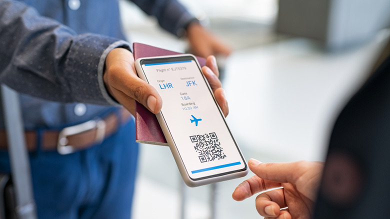 A  person showing an electronic flight ticket on a cellphone to another person