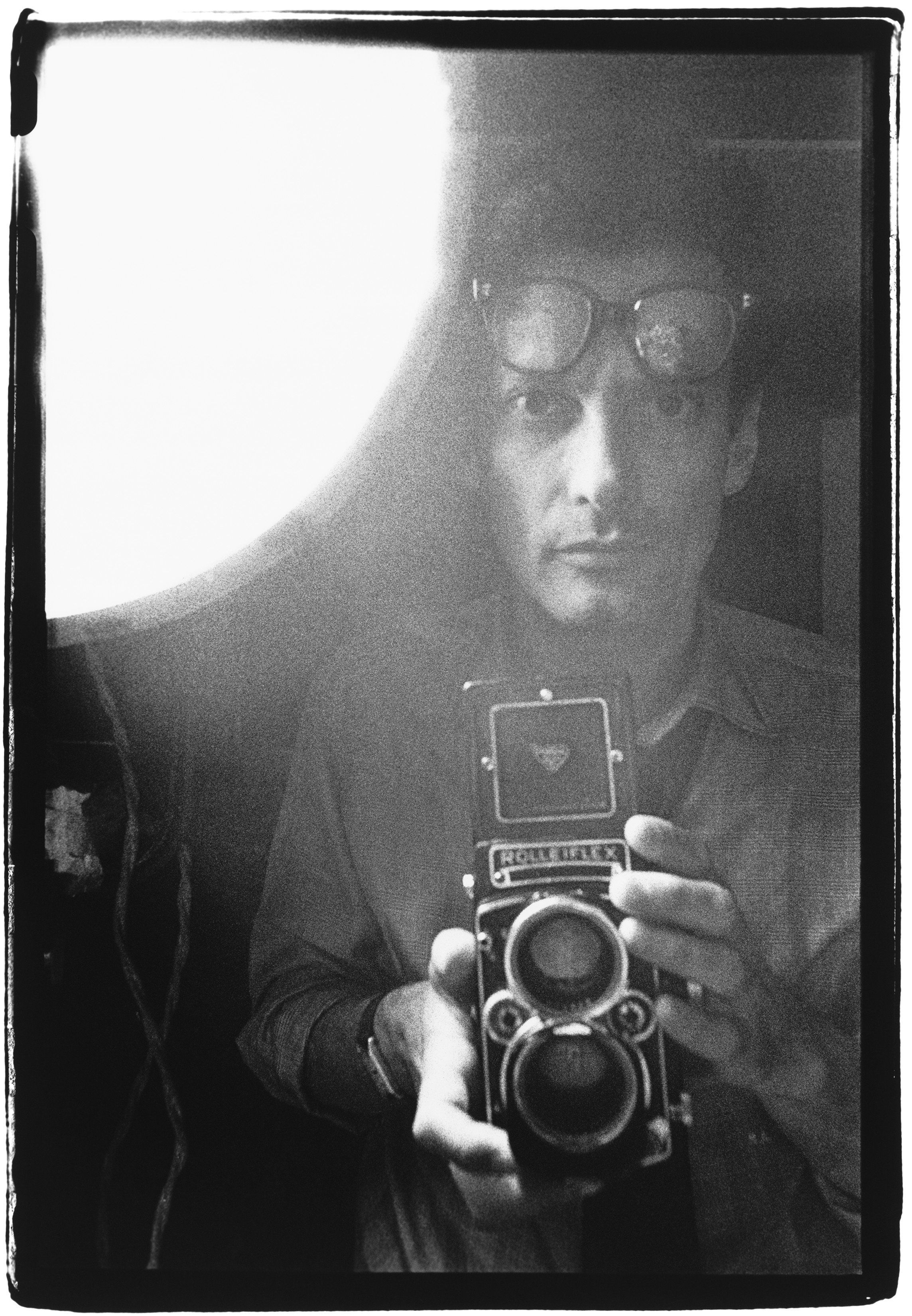 A close-up self-portrait of Richard Avedon grinning broadly, both hands pressed against his temples, the image slightly soft-focused and full of manic energy.