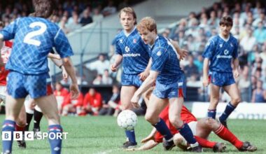 A Chelsea player has control of the ball while a Middlesbrough player attempts to slide tackle him