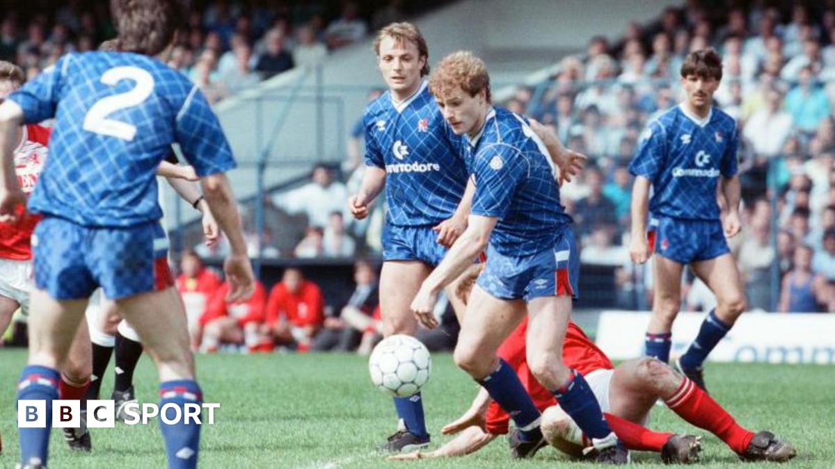 A Chelsea player has control of the ball while a Middlesbrough player attempts to slide tackle him