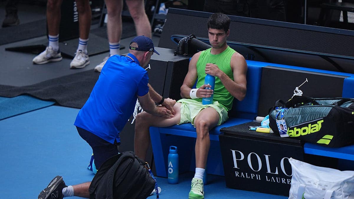 Carlos Alcaraz receiving leg treatment from a trainer during a tennis match.