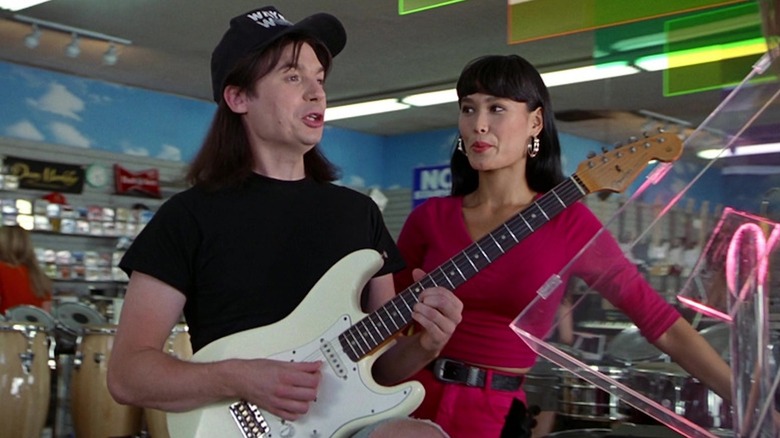 Mike Myers as Wayne Campbell wields a Fender while Tia Carrere as Cassandra Wong looks on in Wayne's World