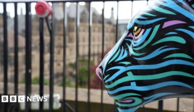 A decorated lion sculpture with blue and purple stripes is situated infront of black railing