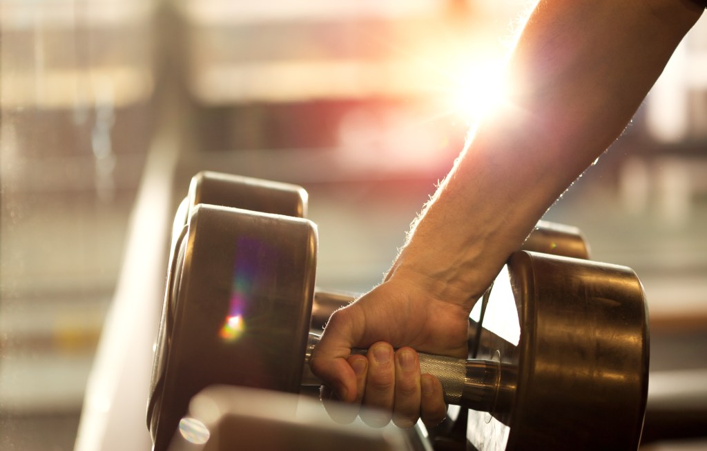 A man's hand grabbing a dumbbell weight with a bright light in the background.