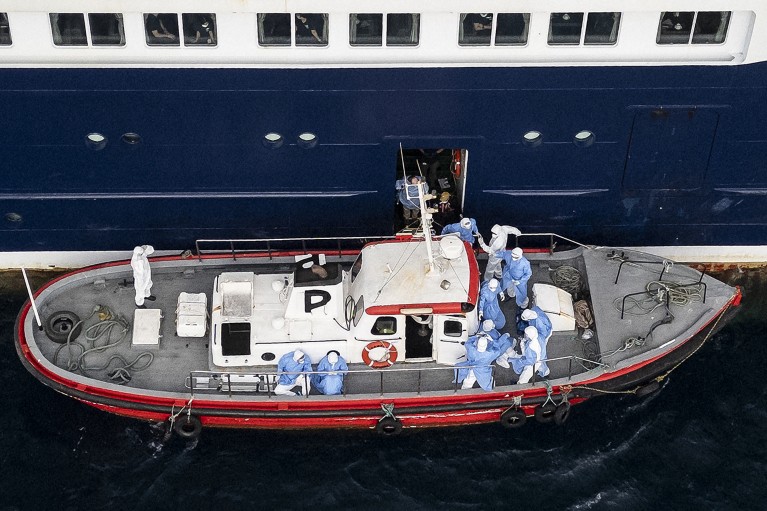 Medical staff in full PPE are seen on a small vessel moored by the side of the cruise ship MV Hondius.