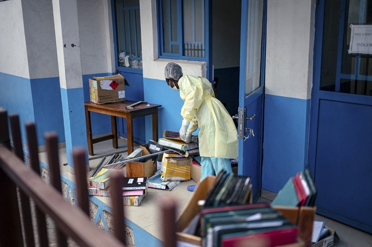 A female worker in PPE is clearing folders and boxes from a room, preparing to take Ebola patients in the DRC.