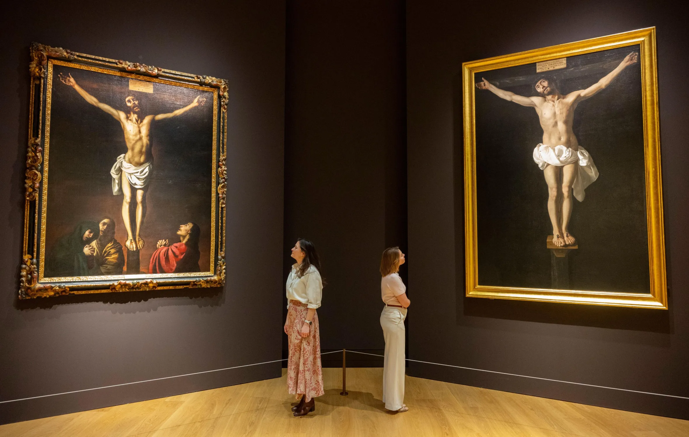 Two women viewing "Christ on the Cross with the Virgin, Mary Magdalene and Saint John" and "The Crucified Christ" paintings at an exhibition.