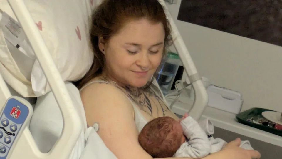 Lauren Evans in a hospital bed holding Ambrose. She is looking down at him.