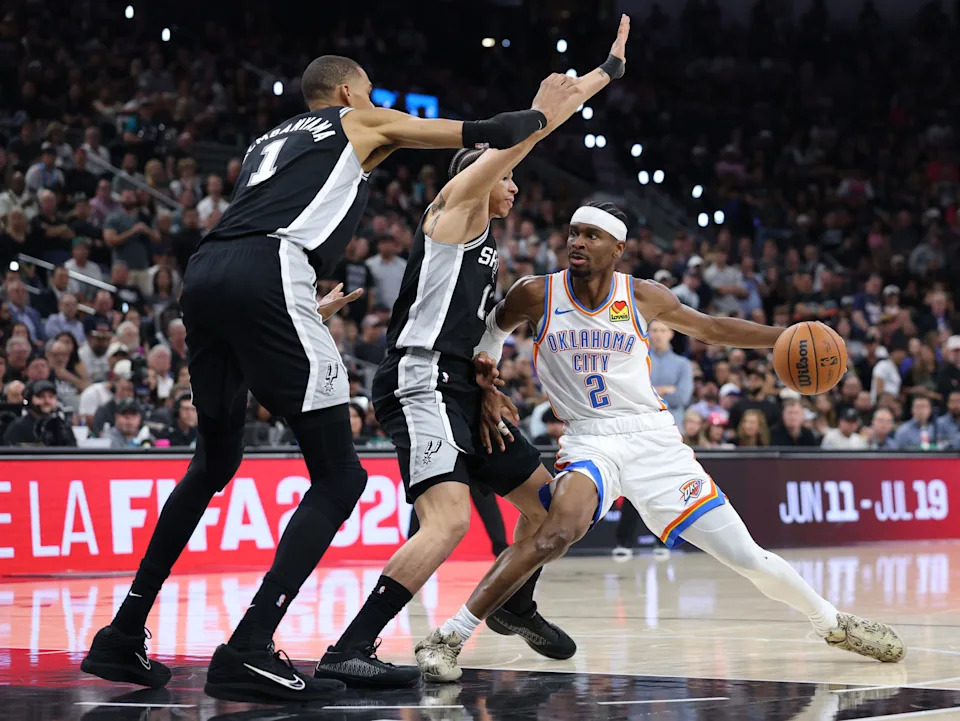 SAN ANTONIO, TEXAS - MAY 28: Shai Gilgeous-Alexander #2 of the Oklahoma City Thunder drives around Carter Bryant #11 and Victor Wembanyama #1 of the San Antonio Spurs during the second quarter in Game Six of the NBA Western Conference Finals at Frost Bank Center on May 28, 2026 in San Antonio, Texas.