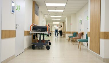 Dark-haired woman and middle-aged man walk along the hospital corridor, in the foreground against the wall is a mobile bed. (Envato Elements)