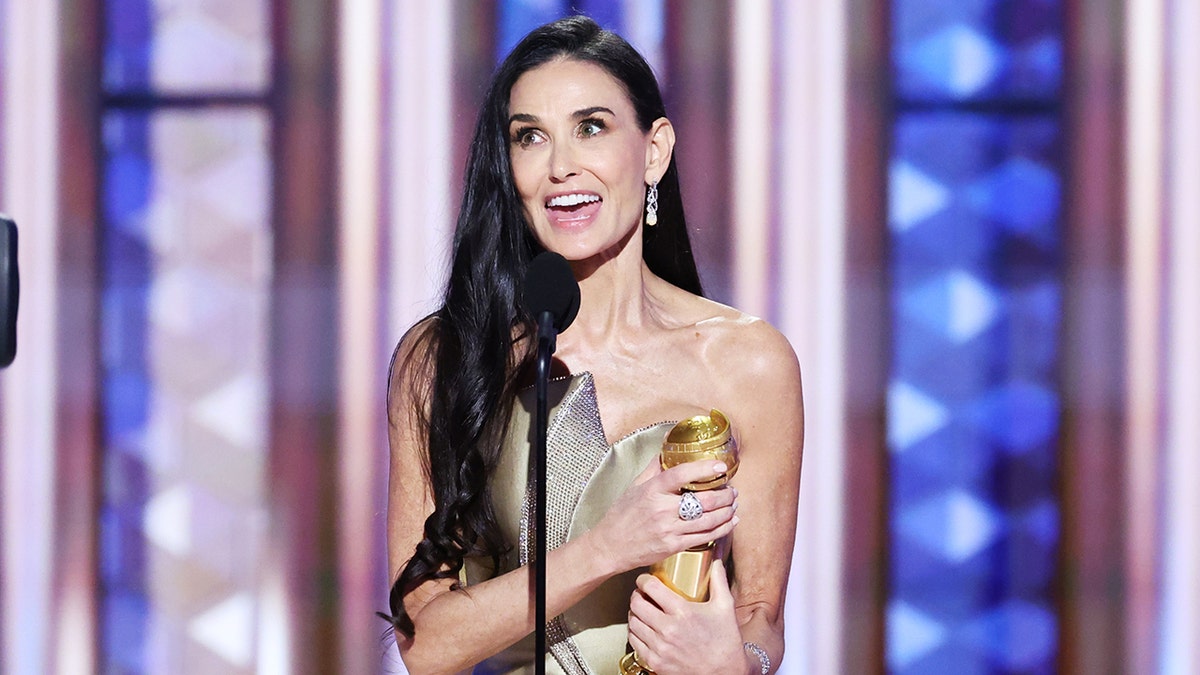 Demi Moore smiling on stage holding a Golden Globe award