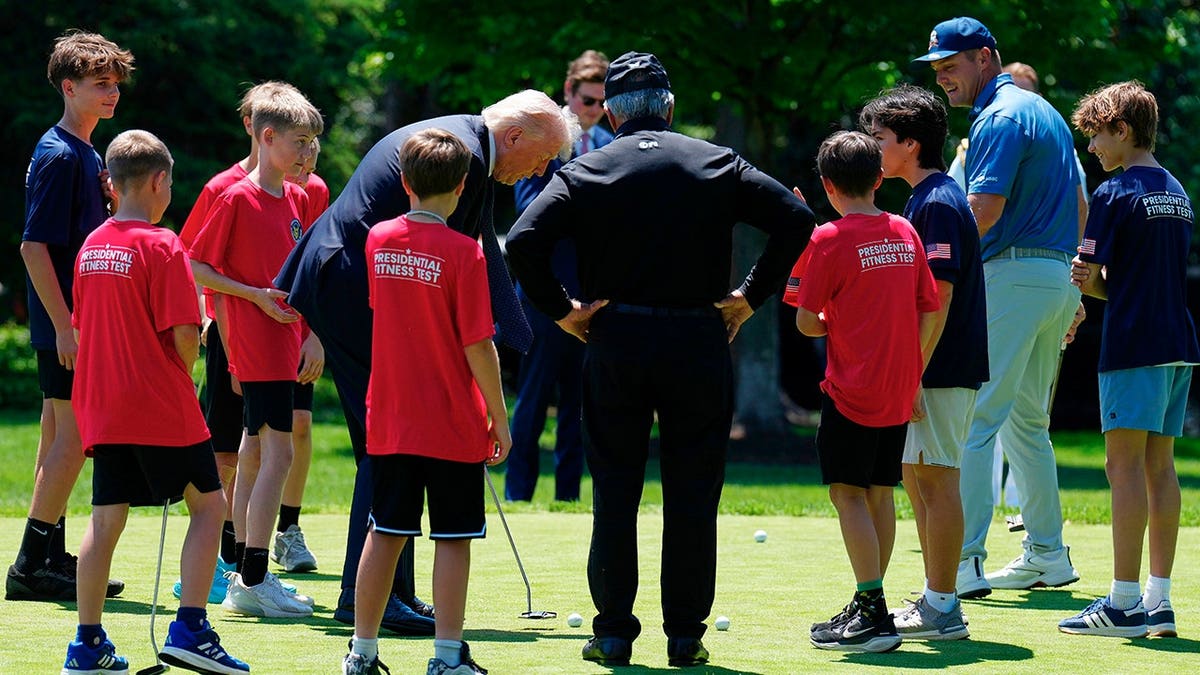 President Donald Trump giving children putting lessons on the White House south lawn with golfers Bryson DeChambeau and Gary Player watching