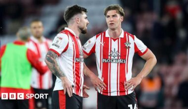 Two Southampton players, wearing red and white striped shirts and black shorts, in conversation