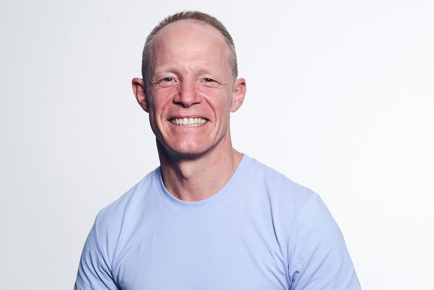 A portrait of a man smiling wearing a light blue T-shirt.
