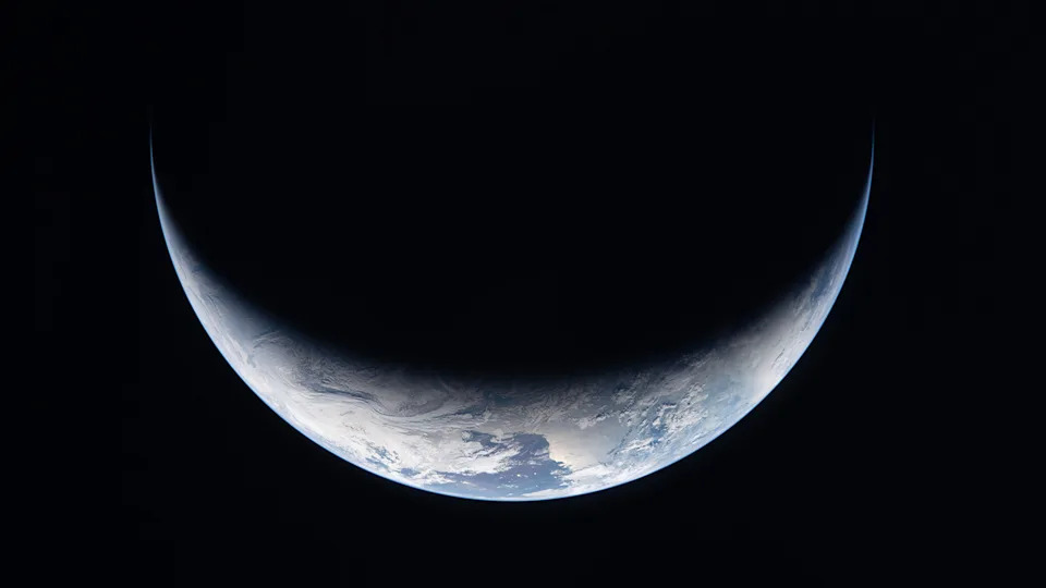 The planet Earth in shadow, its lower curve illuminated in space.