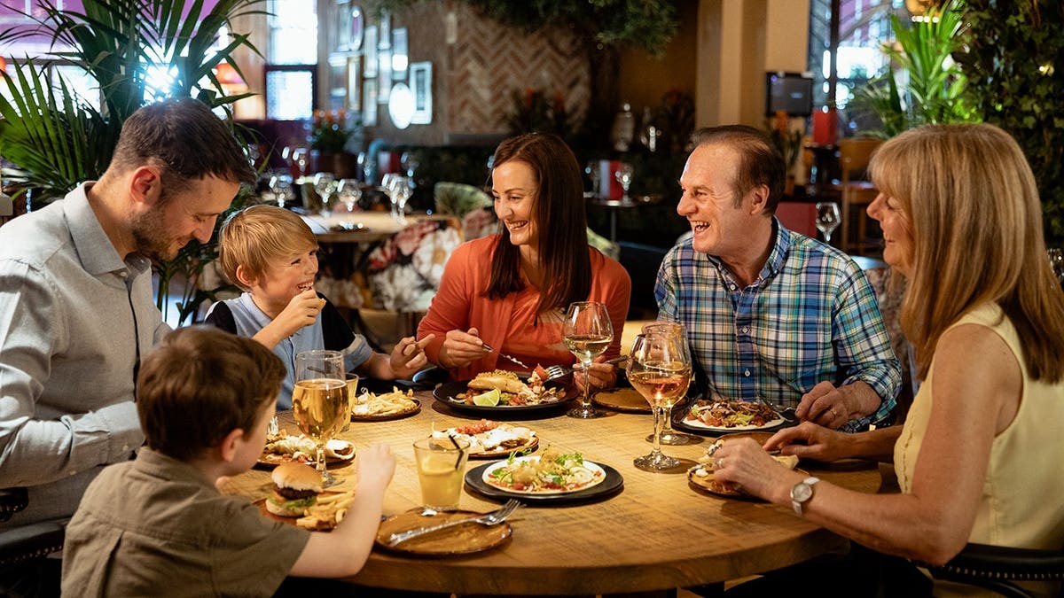 A family laughing and eating together at a restaurant table.