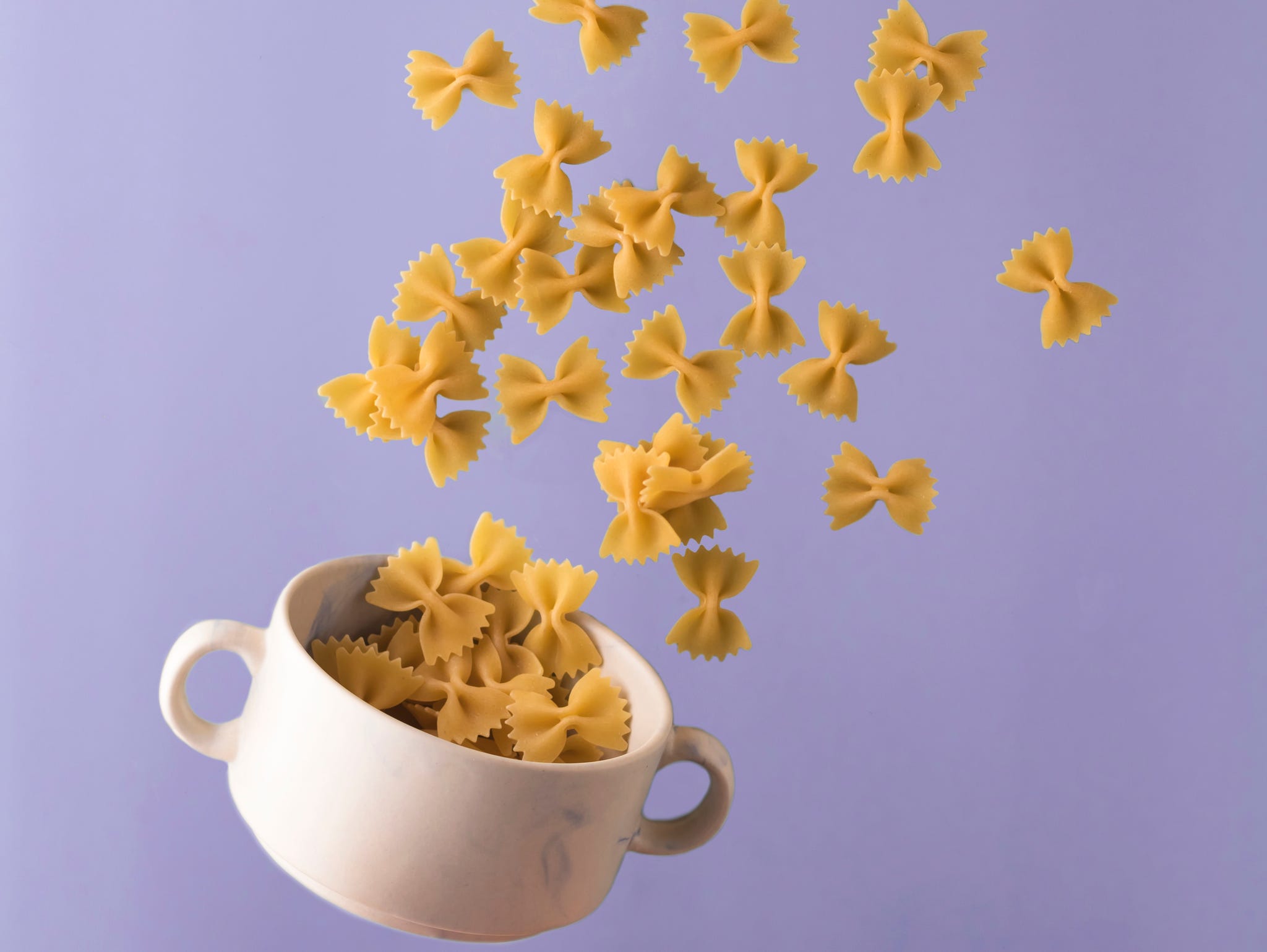 Italian pasta pattern on a bright blue background. Bow tie bowl with pasta. Flying food concept. Levitation. vertical position italian pasta pattern on a bright blue background. bow tie bowl with pasta. flying food concept. levitation. vertical position
