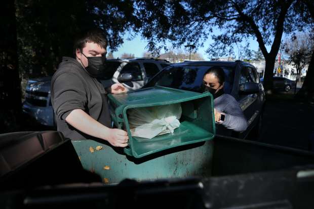 A'Roma Roasters Coffee & Tea employees Cam MacBride, left, and Rosa Rodriguez empty their compost bin into a dumpster in the parking lot of the cafe in Santa Rosa on Wednesday, Jan.19, 2022. Though not accepted from residential users outside the city of Sonoma, compostable bags are allowed in large commercial green waste dumpsters. (Beth Schlanker/The Press Democrat)
