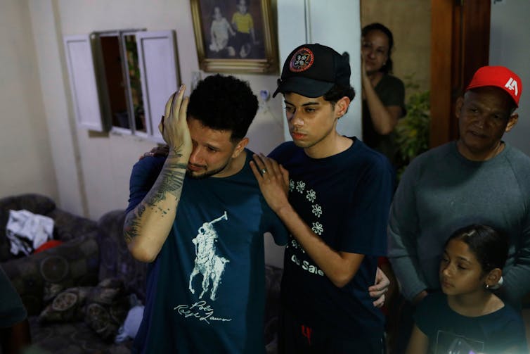 A dark-haired man wipes his eyes as a teenaged boy embraces him.