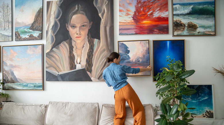 A woman hanging fine art on a wall in her home.