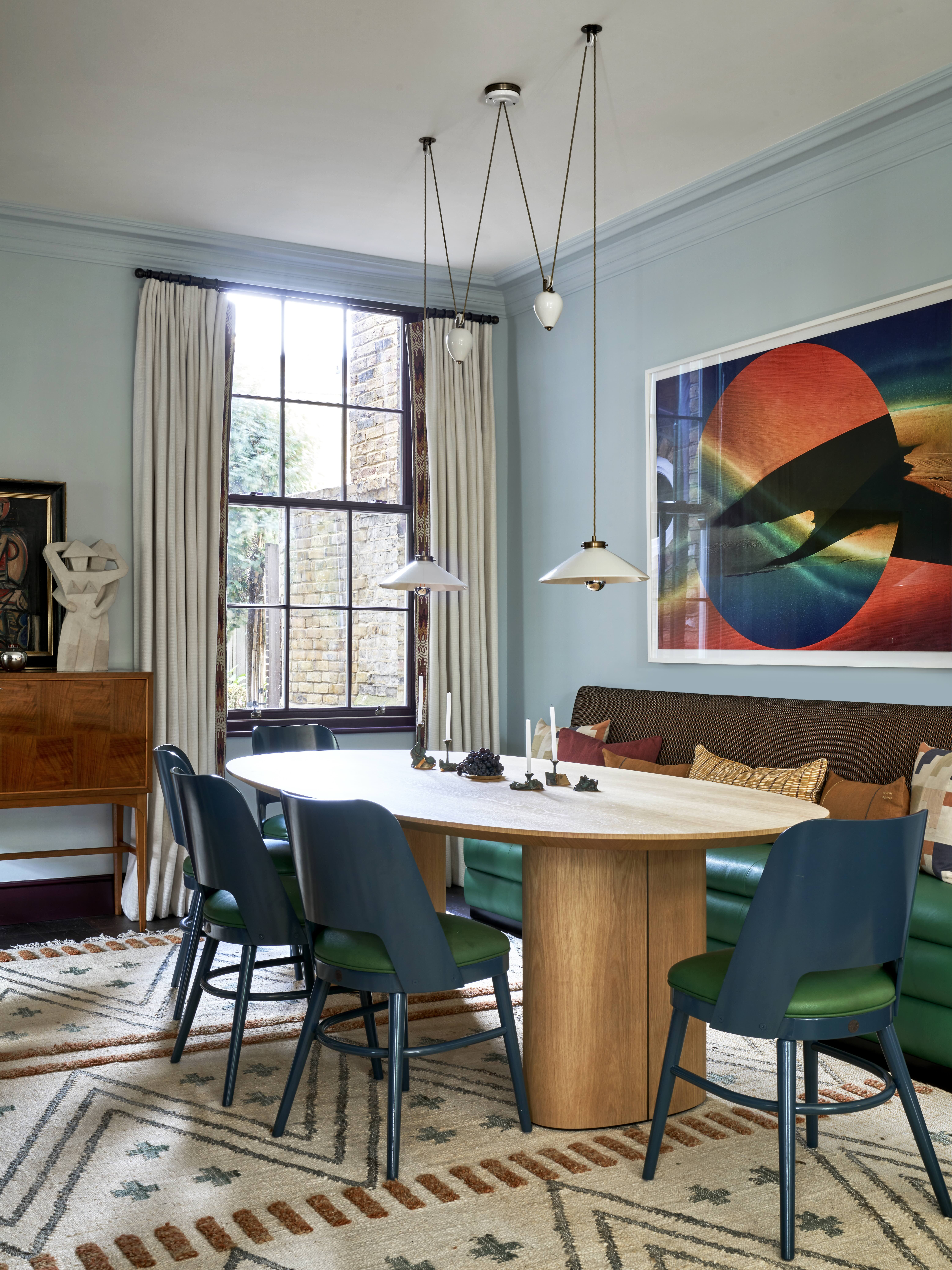 A contemporary dining room painted in mineral blue with colorful artwork and a table in front of a window