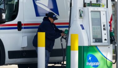 A woman holds a fuel pump nozzle to fill up a USPS vehicle's tank at a gas station, in Chicago, Tuesday, April 7, 2026. (AP Photo/Nam Y. Huh)