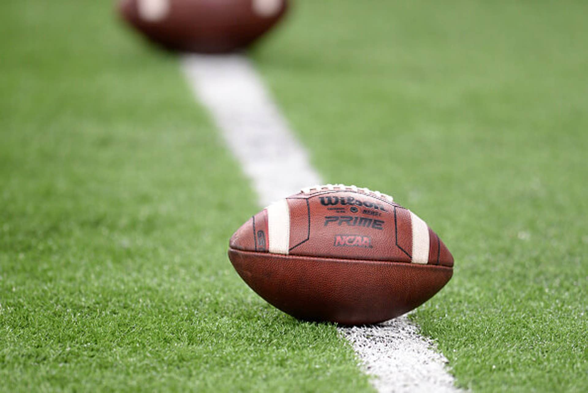 A Wilson football displays a NCAA logo as it sits on a football field.
