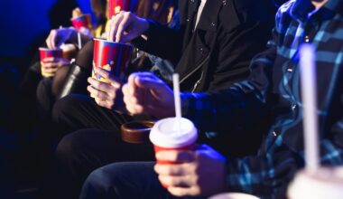 Glasses with a tube and popcorn in the hands of people in a movie theater close-up.