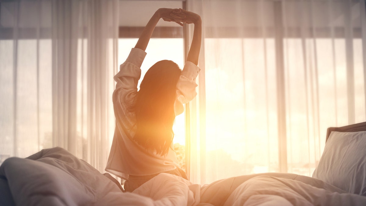 Happy woman stretching in bed after waking up
