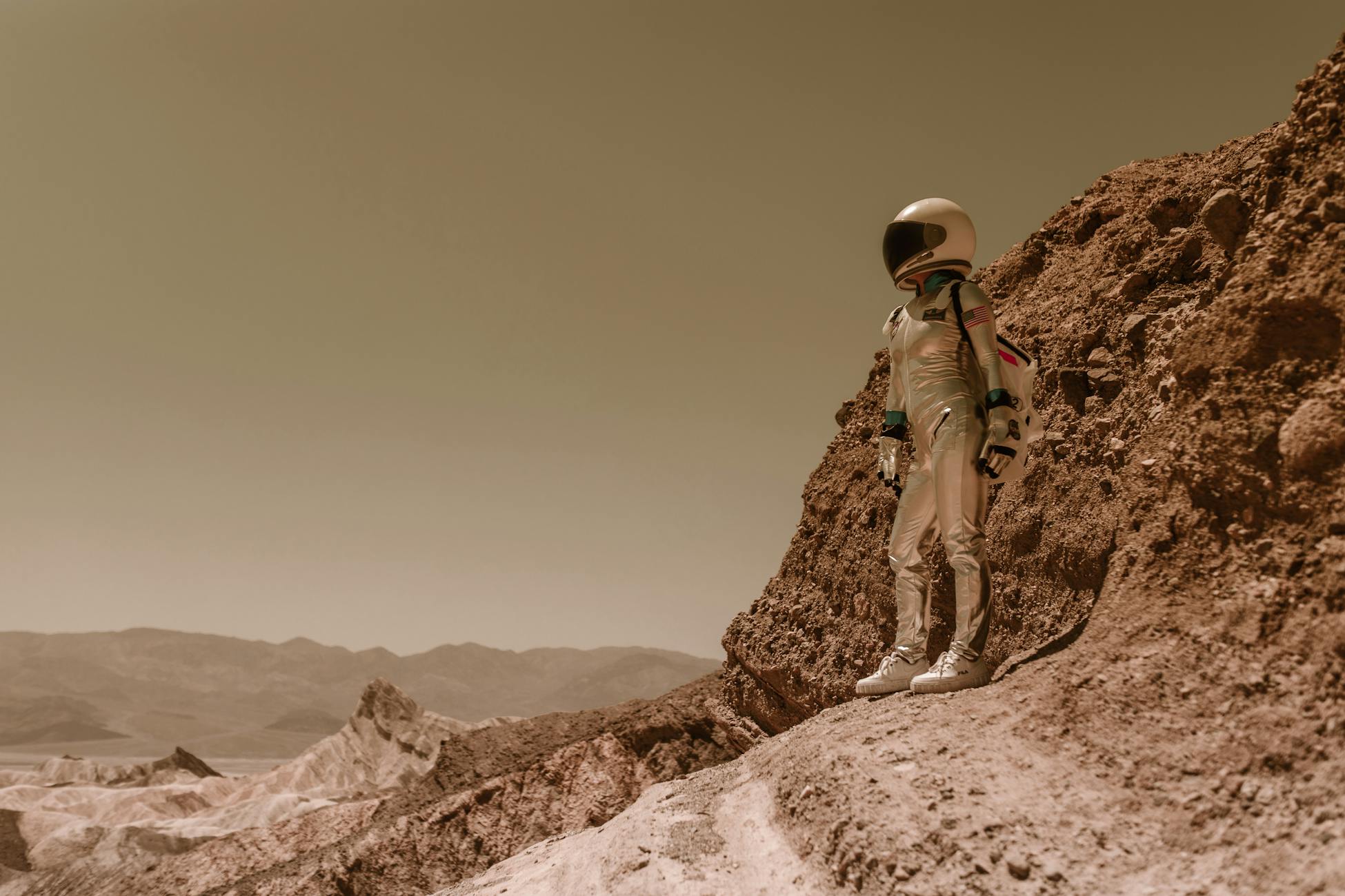 A lone astronaut in a spacesuit stands on a rugged, rocky terrain resembling an alien planet.