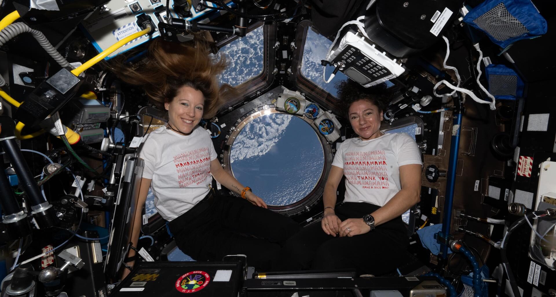 From left, Expedition 74 flight engineers Sophie Adenot of ESA (European Space Agency) and Jessica Meir of NASA pose for a portrait inside the International Space Station's cupola on Mother's Day. Adenot, who has a son, and Meir, who has a daughter, wear T-shirts celebrating motherhood.
