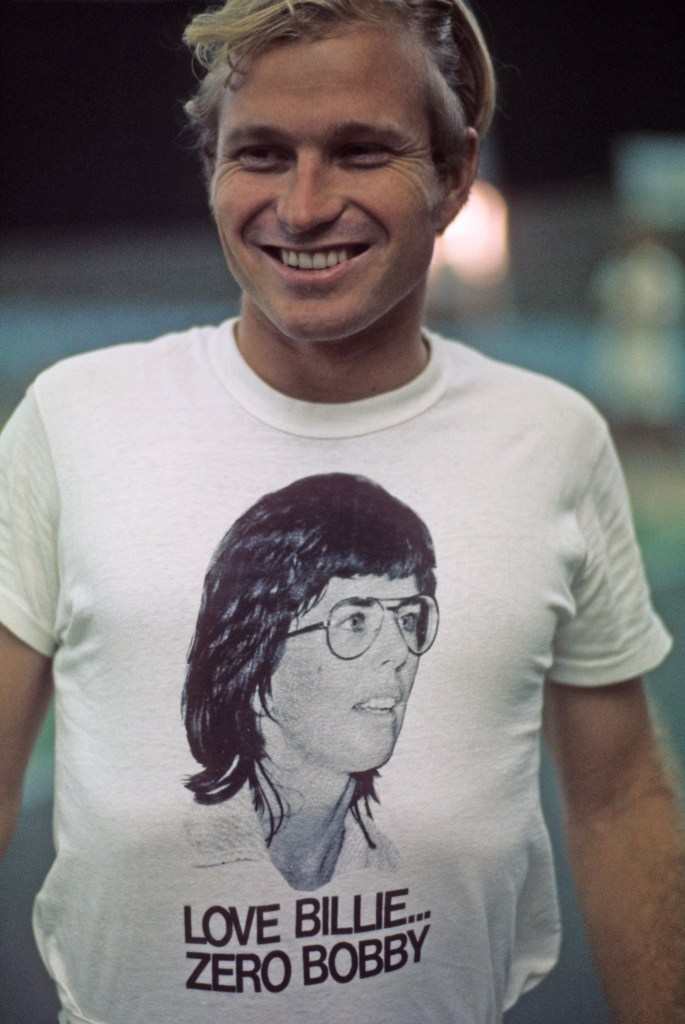 Larry King, husband of Billie Jean King, smiling and wearing a white t-shirt with a picture of Billie Jean King and the slogan "Love Billie... Zero Bobby."