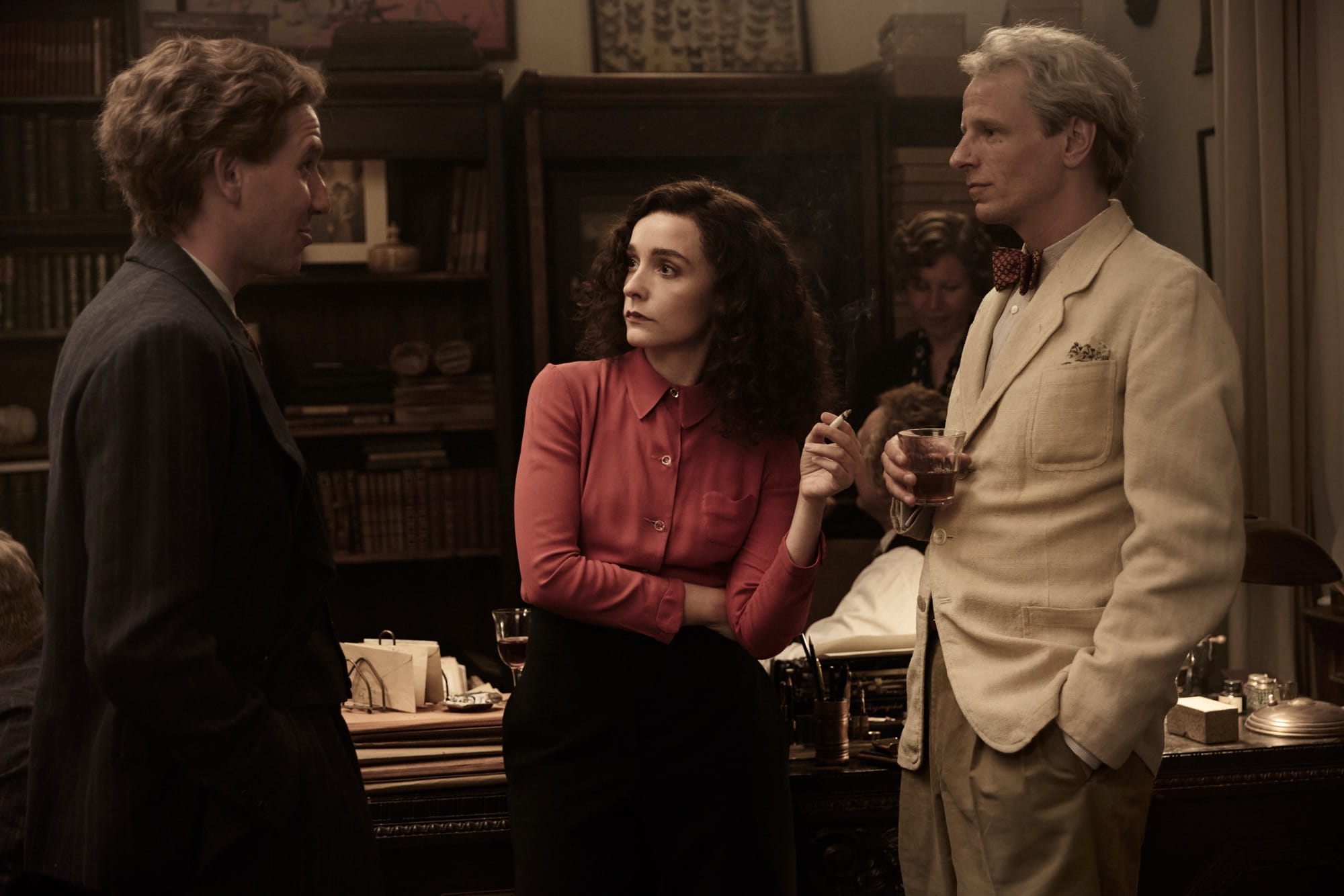 a white woman with dark curly hair standing between two white men