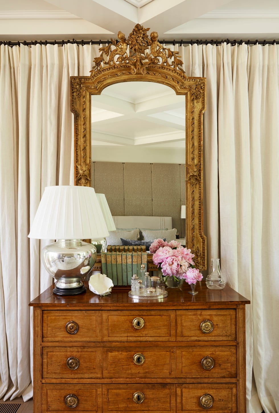 cream linen panels form a soft backdrop for a gilded mirror in the bedroom