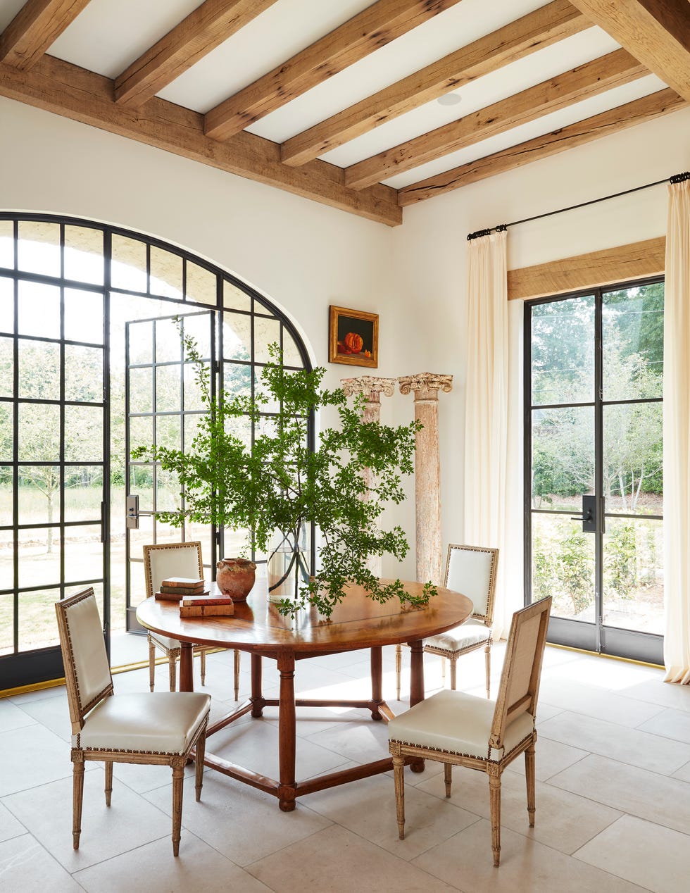 a limestone dining room with a round stretcher base table by bobby mcalpine