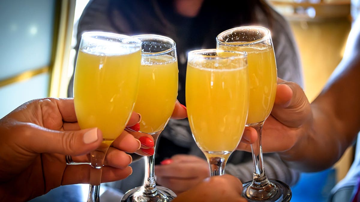 A close-up view of a group of friends raising mimosa glasses in a toast at brunch.