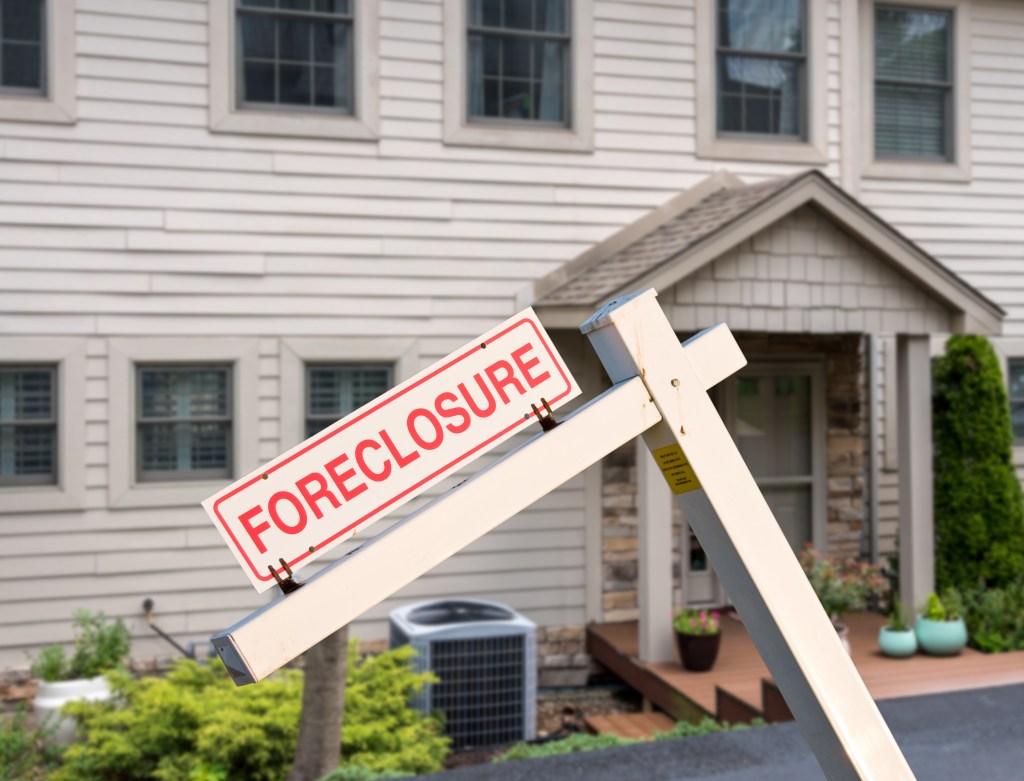Sign that says foreclosure on a bent stick in front of a white house.
