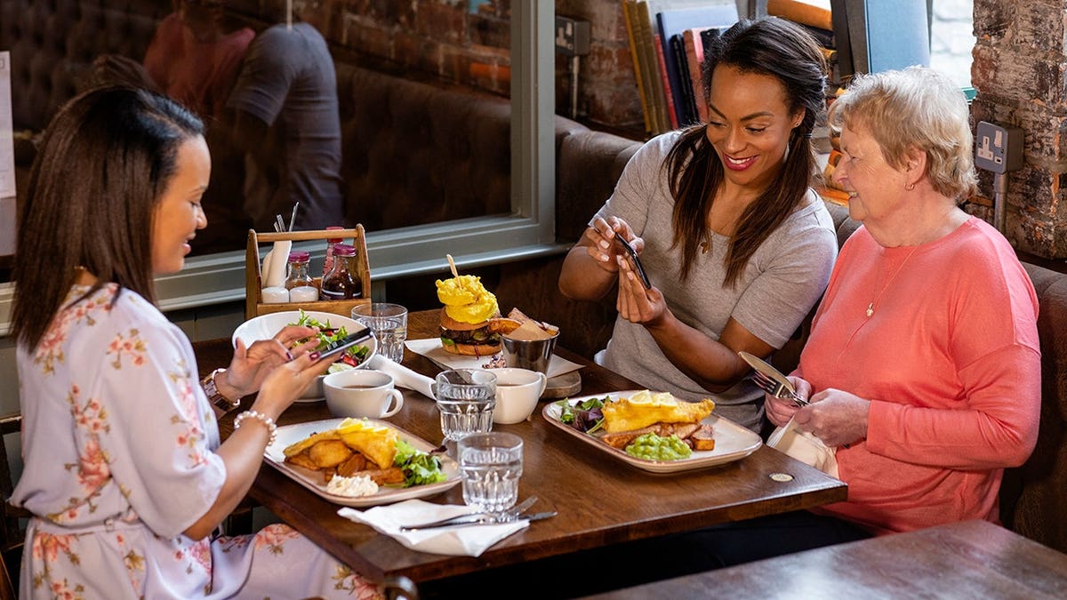 A woman and her two daughters sitting at a restaurant table using mobile phones.
