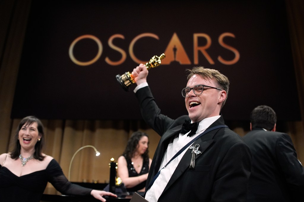 Pavel Talankin holding up an Oscar award while smiling broadly.