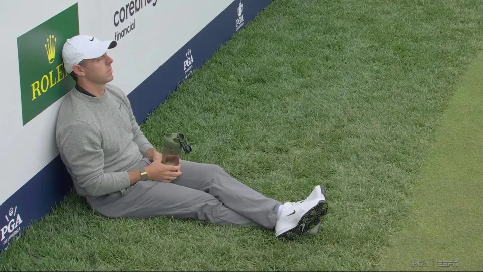 Rory McIlroy is slumped against the advertising board after being forced to wait.