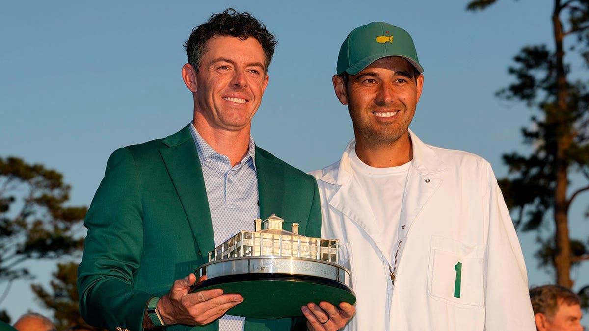 Rory McIlroy posing with caddie Harry Diamond holding Masters trophy at Augusta National Golf Club