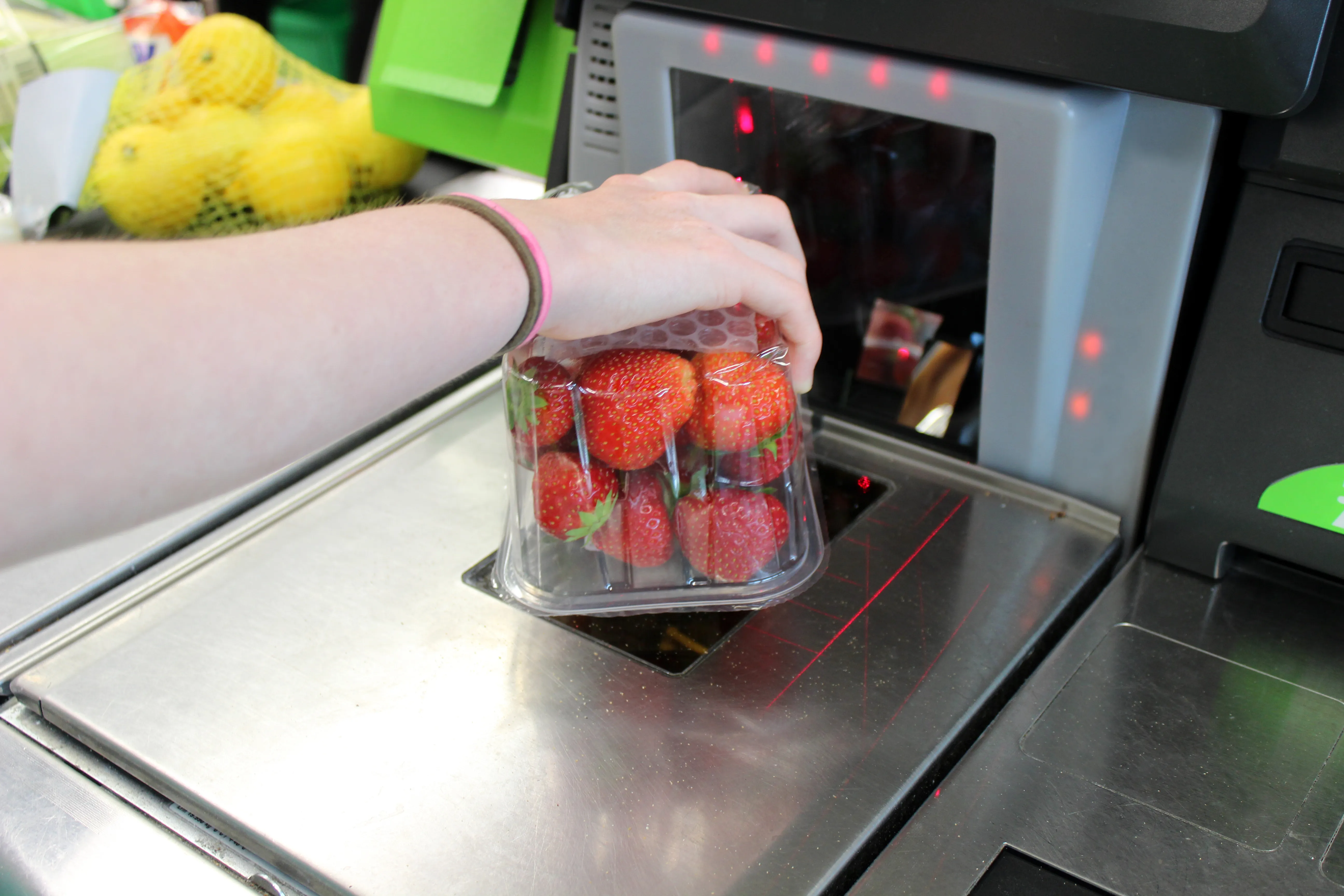 A person's hand scans a clear plastic container of strawberries at a self-service checkout till.