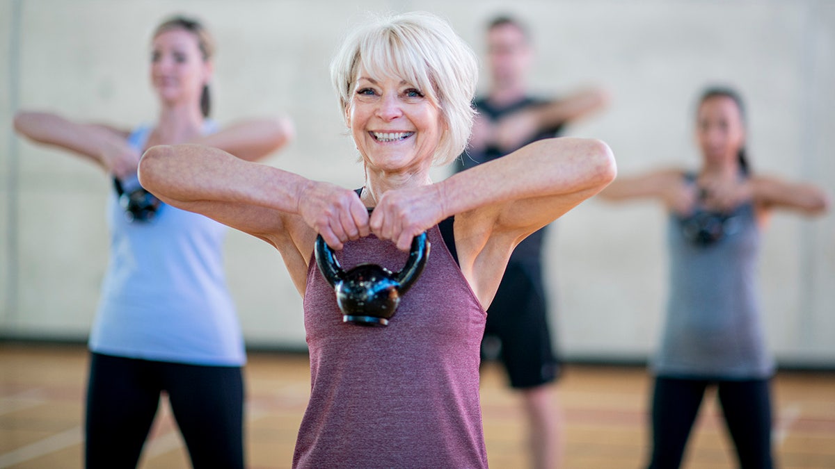 Older Caucasian woman doing a squat with a kettlebell in a fitness class