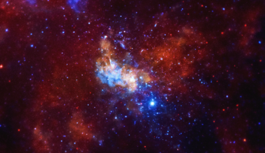 A Chandra X-ray Observatory image around the Sagittarius A* supermassive black hole, located in the center of the Milky Way galaxy, is shown. The image is dominated by vibrant red and blue hues, with a large amount of celestial objects visible. At the center of the image, there is a bright, lumpy object showing the intense X-ray radiation emanating from the Sgr A* black hole. In the surrounding area, there are a couple smaller lumps layered throughout the image, feathering out to a large almost butterfly shape filling much of the screen. The image appears textured, like dozens of blue and orange glow worms are paused in their wriggling. The image offers an unprecedented view of lobes of hot gas extending for a dozen light years on either side of the black hole. These lobes provide evidence for powerful eruptions occurring several times over the last ten thousand years. The image also contains several mysterious X-ray filaments, some of which may be huge magnetic structures interacting with streams of energetic electrons produced by rapidly spinning neutron stars. Such features are known as pulsar wind nebulas.