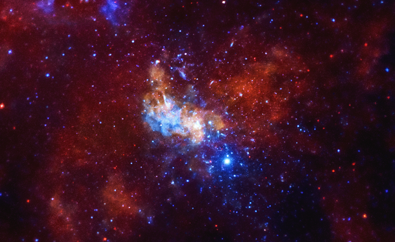 A Chandra X-ray Observatory image around the Sagittarius A* supermassive black hole, located in the center of the Milky Way galaxy, is shown. The image is dominated by vibrant red and blue hues, with a large amount of celestial objects visible. At the center of the image, there is a bright, lumpy object showing the intense X-ray radiation emanating from the Sgr A* black hole. In the surrounding area, there are a couple smaller lumps layered throughout the image, feathering out to a large almost butterfly shape filling much of the screen. The image appears textured, like dozens of blue and orange glow worms are paused in their wriggling. The image offers an unprecedented view of lobes of hot gas extending for a dozen light years on either side of the black hole. These lobes provide evidence for powerful eruptions occurring several times over the last ten thousand years. The image also contains several mysterious X-ray filaments, some of which may be huge magnetic structures interacting with streams of energetic electrons produced by rapidly spinning neutron stars. Such features are known as pulsar wind nebulas.
