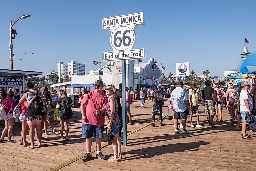 Crowd of tourists surround the road sign for the end of the famous Route 66 on the Santa Monica Pier.