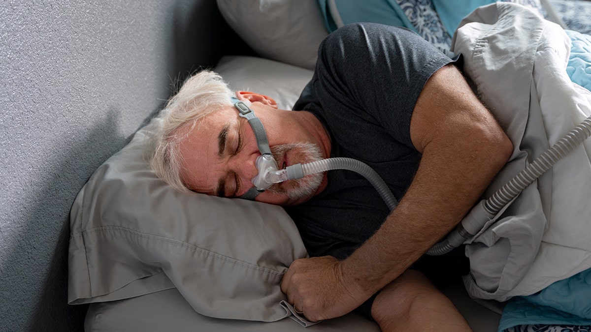 A man sleeping in bed using a CPAP machine for sleep apnea treatment