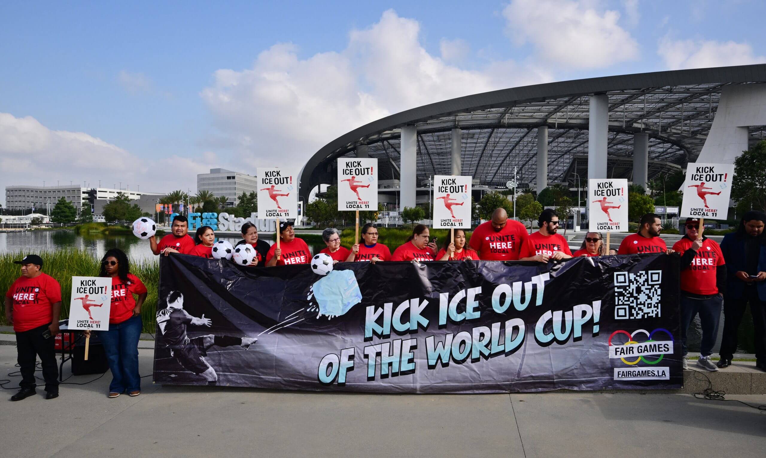 SoFi Stadium workers holding anti-ICE placards and a sign reading "Kick ICE out of the World Cup" in front of the stadium