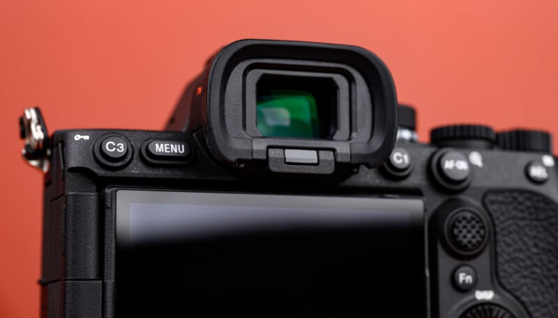 Close-up of the back of a digital camera showing its viewfinder, several control buttons, and part of the LCD screen, with an orange background.